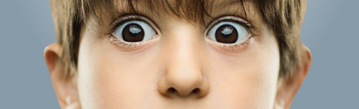 Focused image of a young boy with his eyes wide open under brown hair.