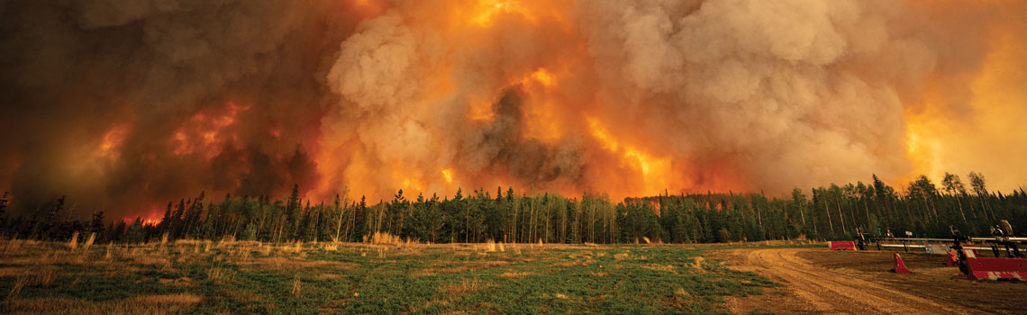 photograph of a fire burning in Alberta, the sky is completely blocked out with smoke