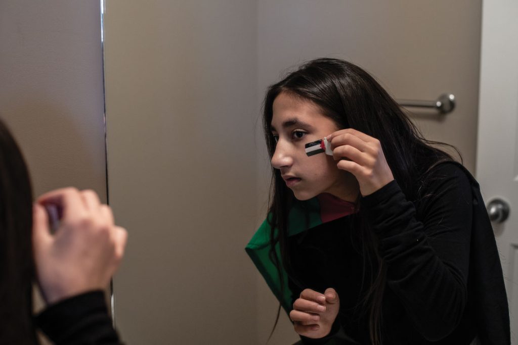 Zeher looking in a mirror to paint a flag on her cheek
