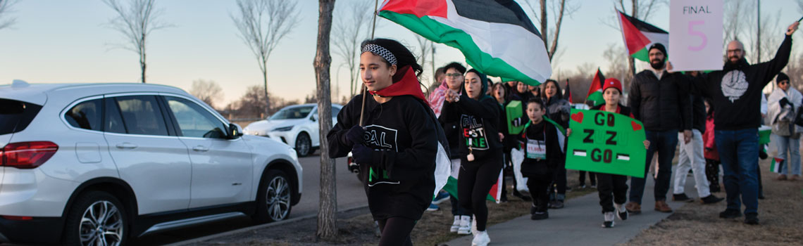 Zeher Assaf running while holding a Palestinian flag while people behind her cheer