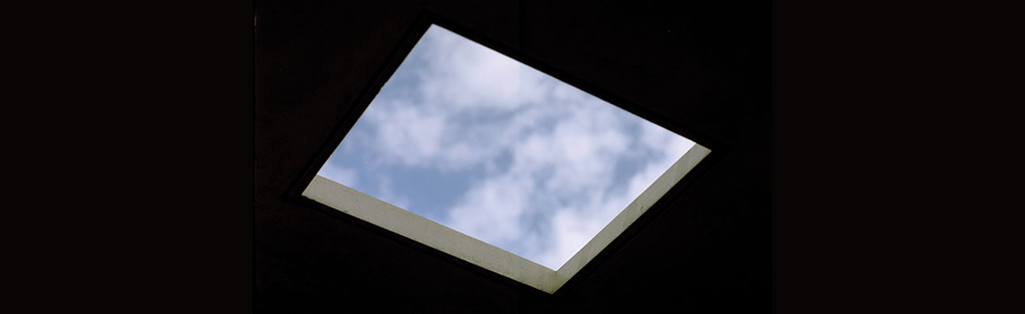 Optimism in neoliberalism. A dark room with a square cut out of the ceiling. blue sky is above.