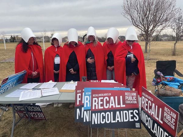 6 Campaign volunteers dressed as handmaidens in red with a white visor.
